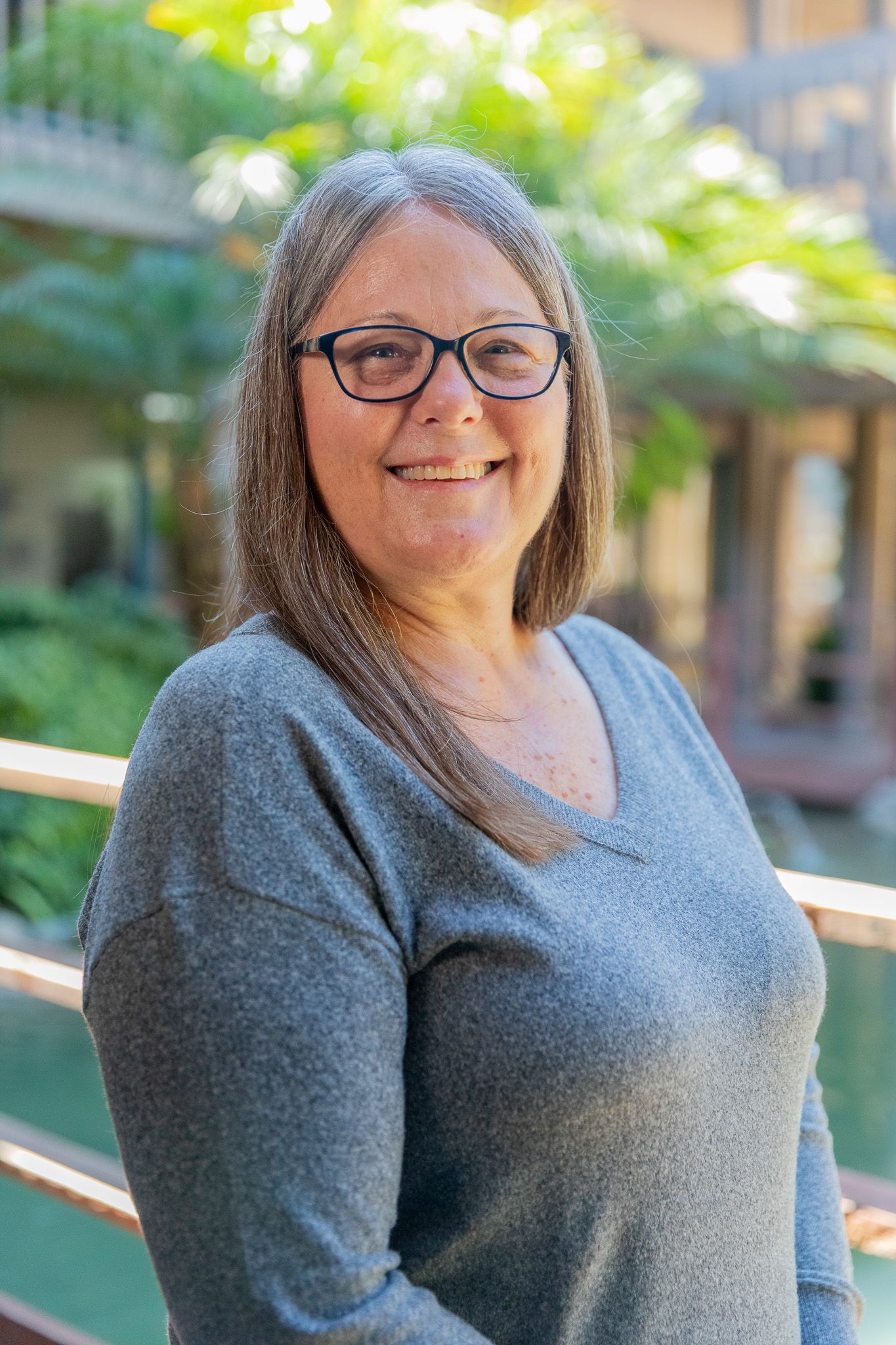 A woman wearing glasses and a gray jacket is smiling for the camera.