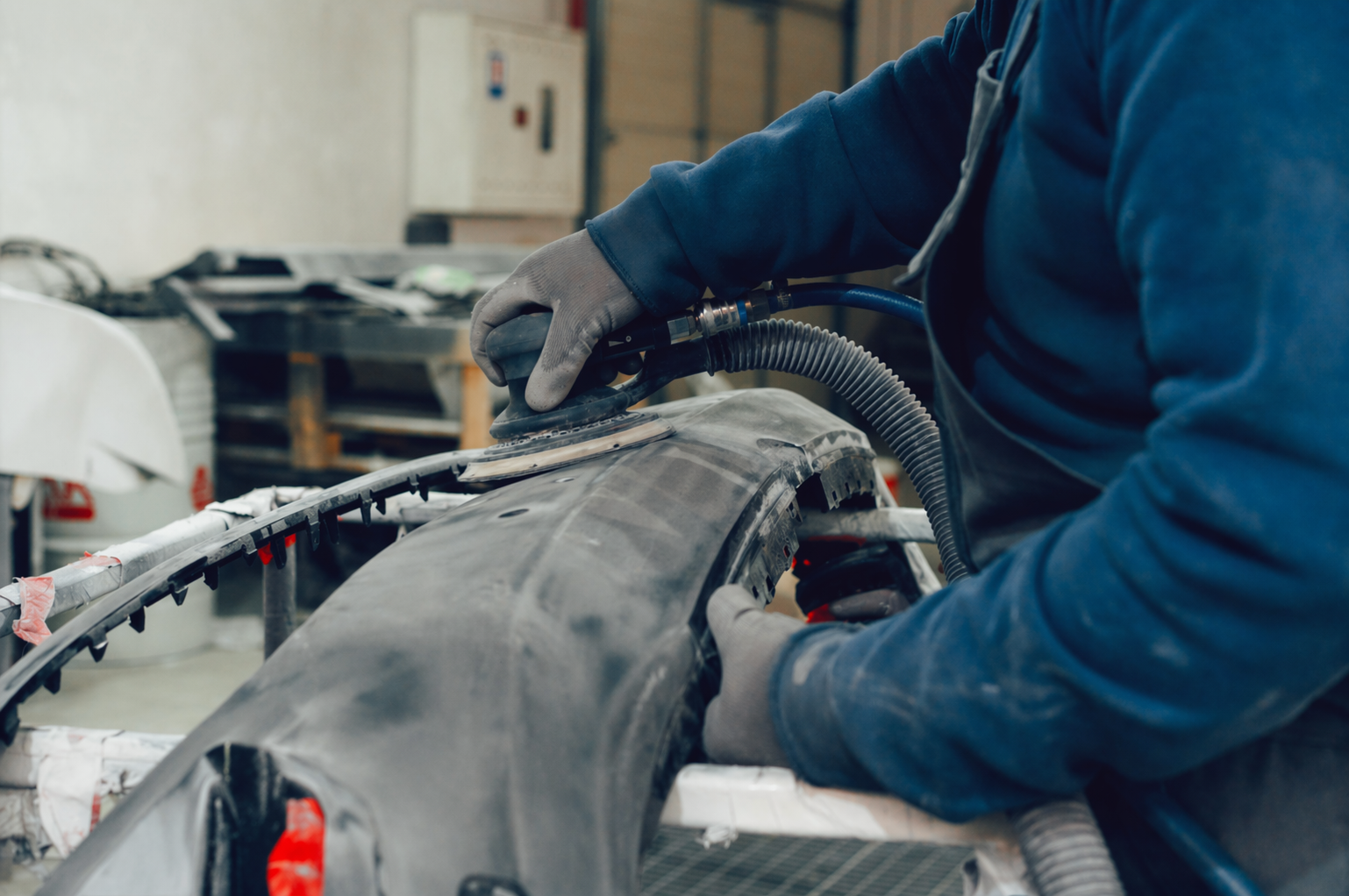 Meccanico in giacca blu ripara il motore di un'auto in un'officina.