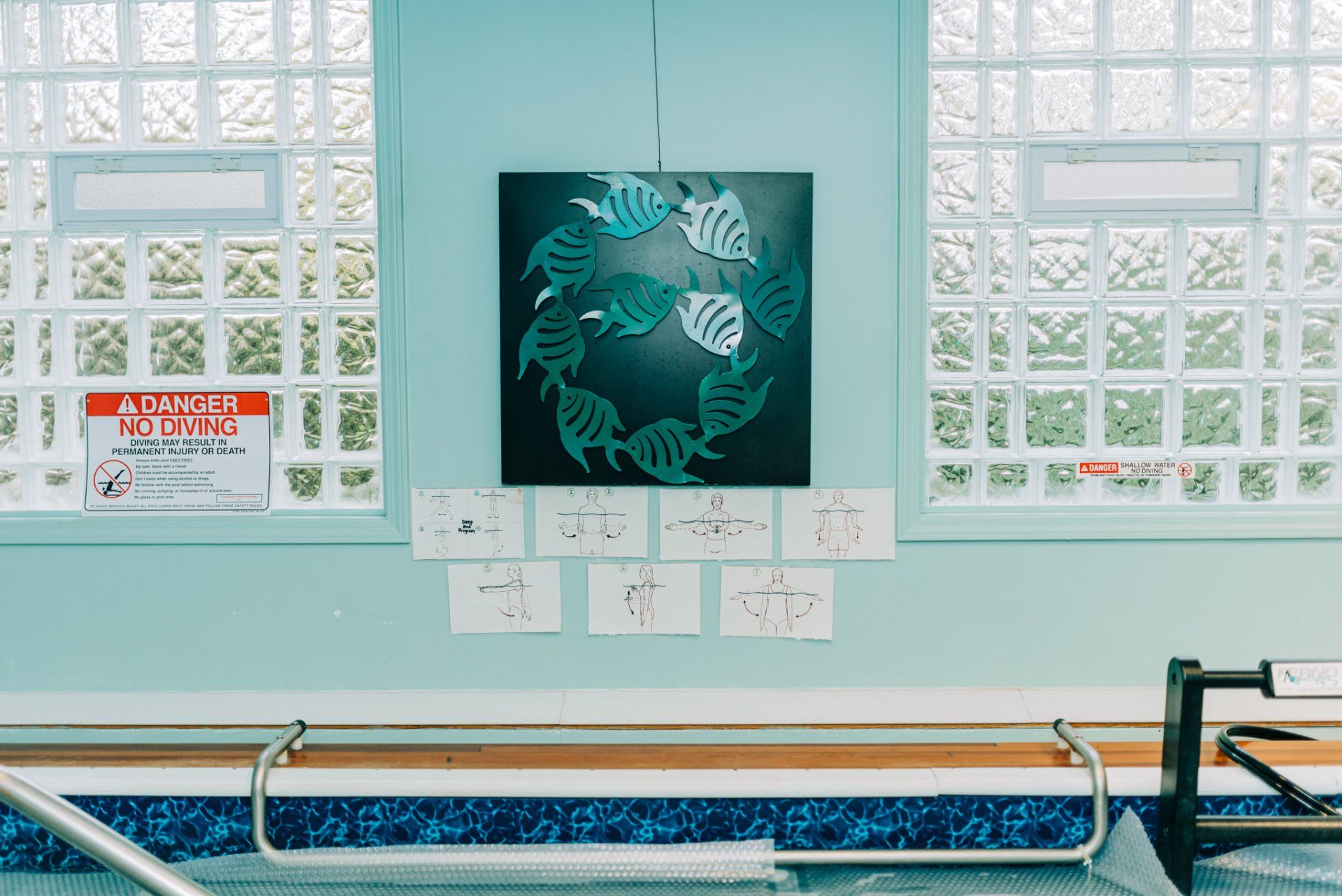 A painting of fish is hanging on a wall next to a swimming pool.