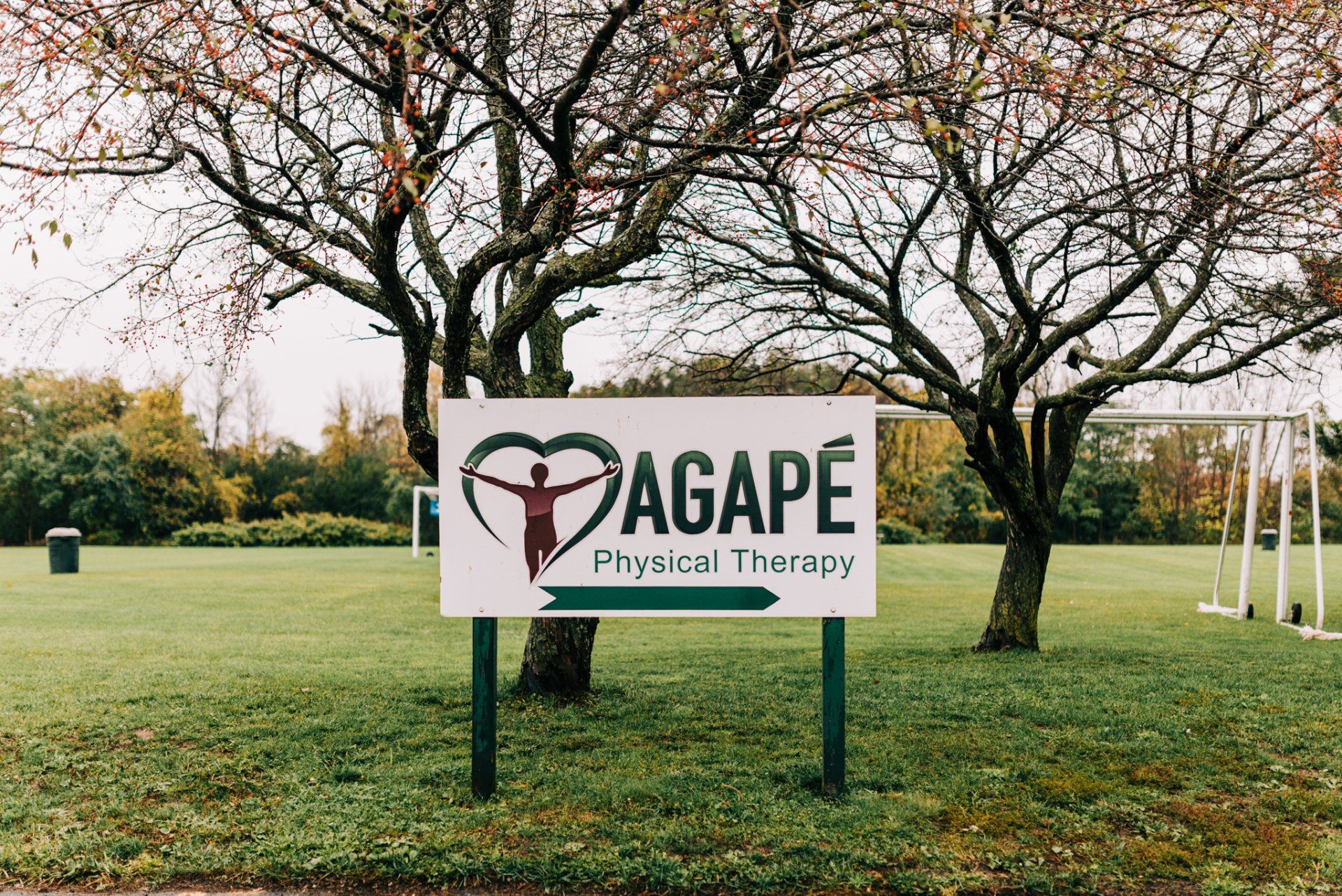 A sign for agape physical therapy is in the middle of a grassy field.