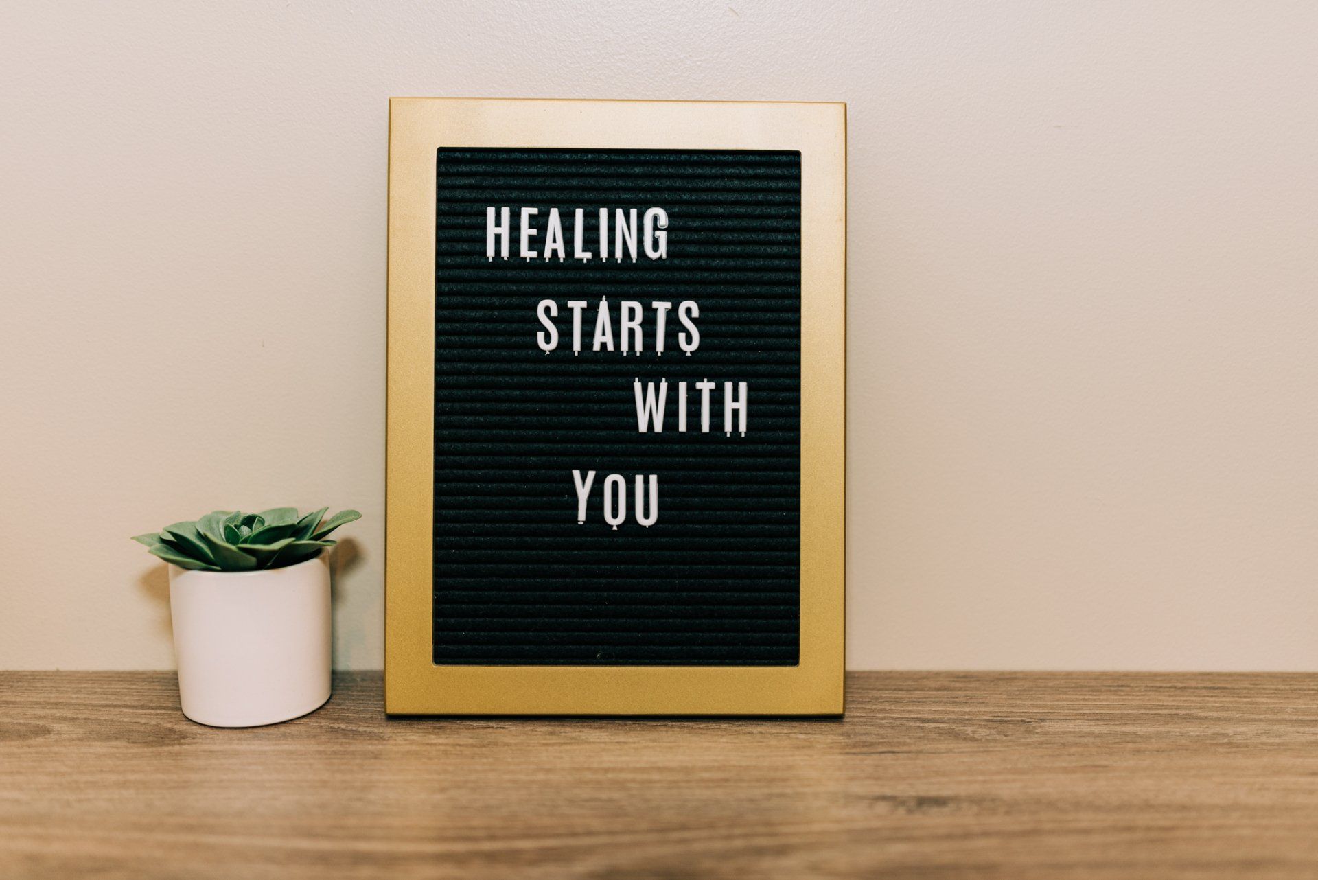 A sign that says `` healing starts with you '' is sitting on a wooden table next to a potted plant.