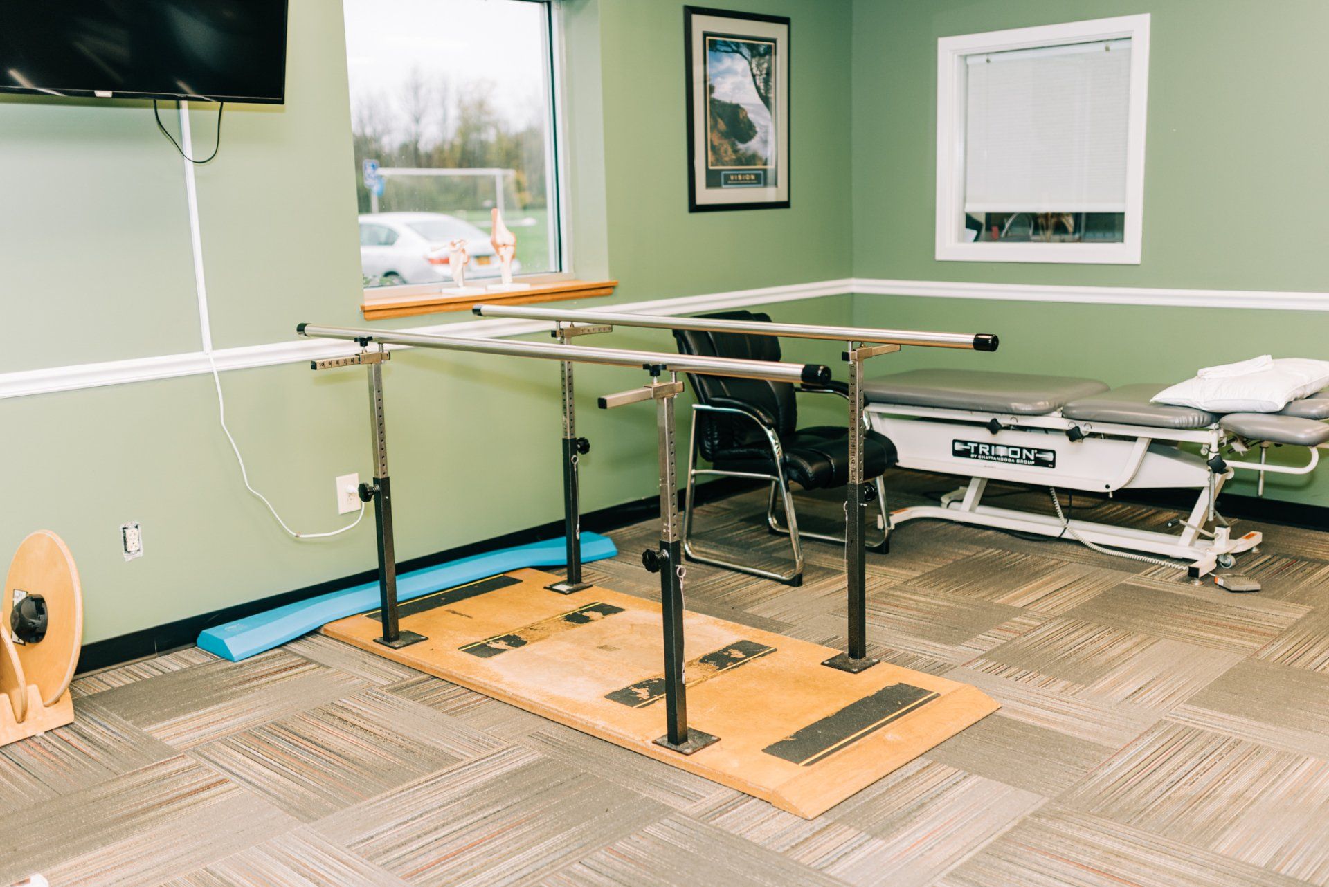 A physical therapy room with parallel bars , a table , and a television.