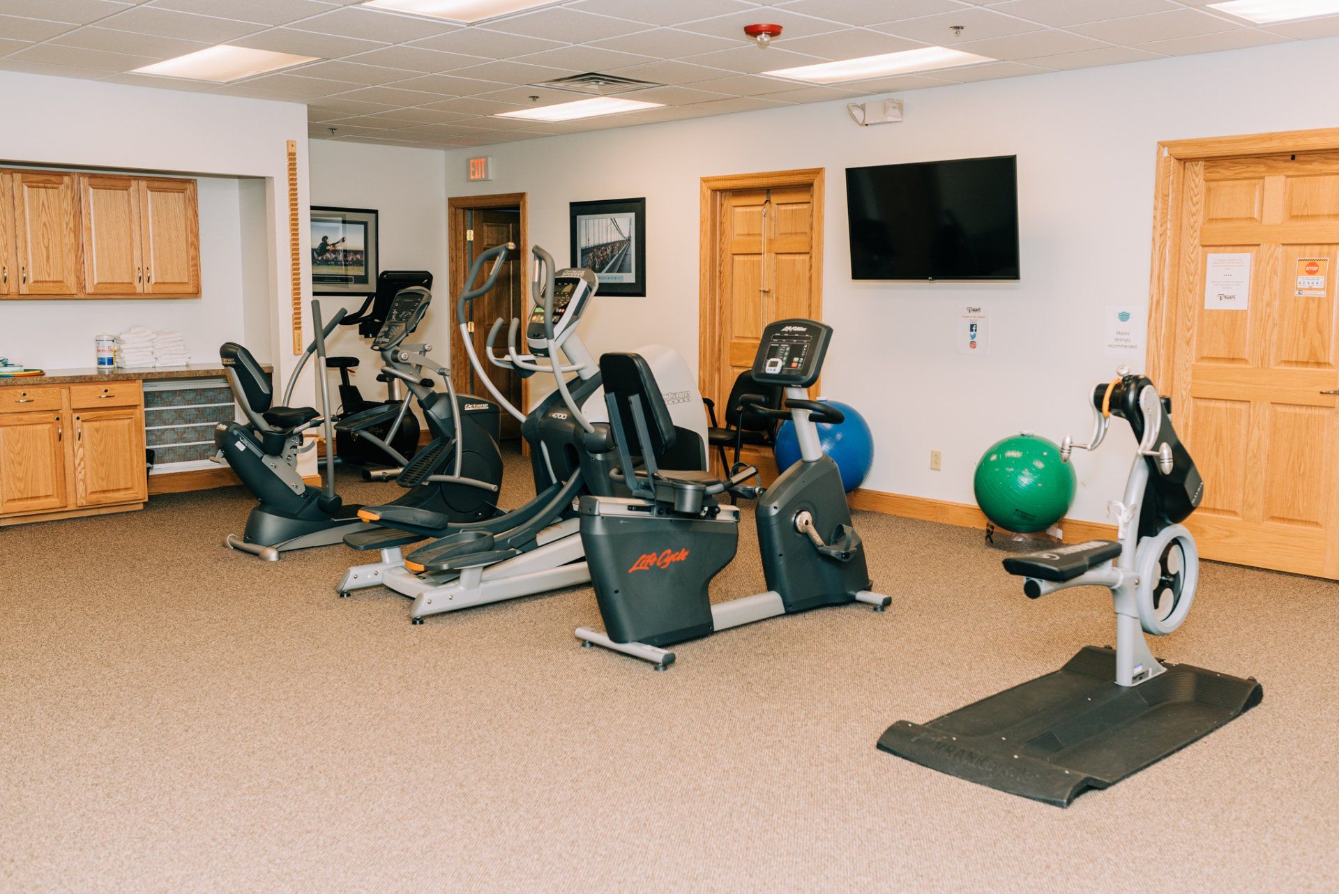 A gym with a lot of exercise equipment and a tv on the wall.