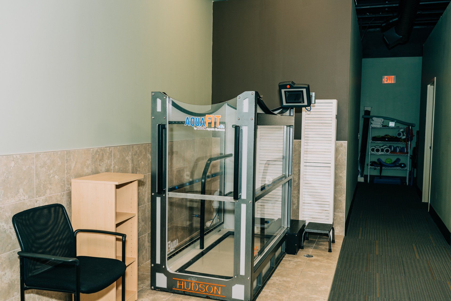 A treadmill is sitting in a hallway next to a chair.