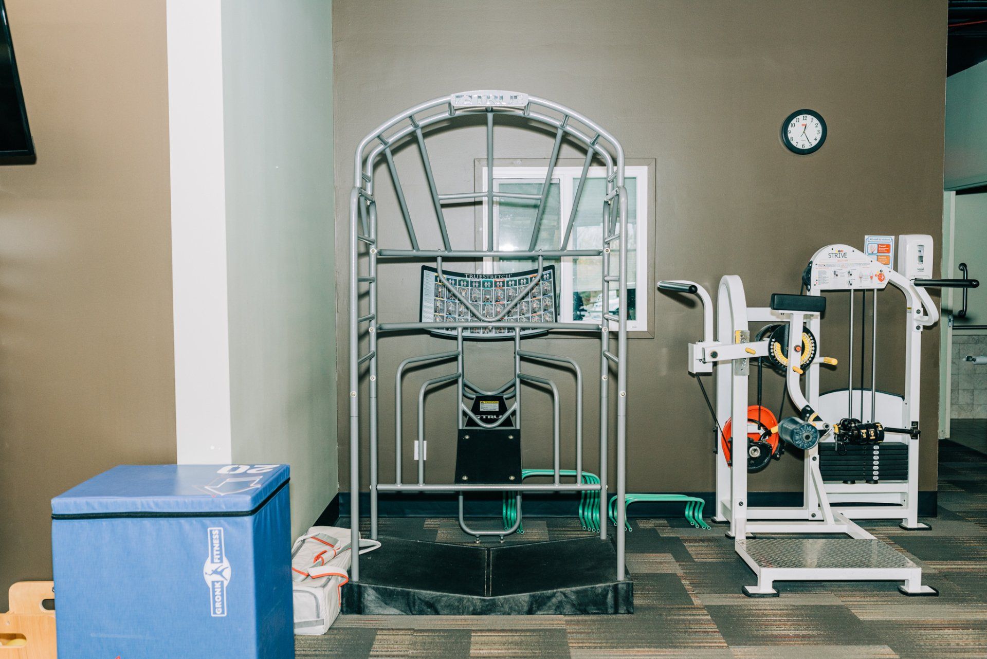 A gym with a lot of exercise equipment and a clock on the wall.