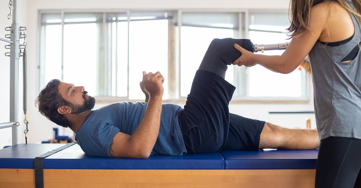 A woman is helping a man stretch his legs on a pilates mat.