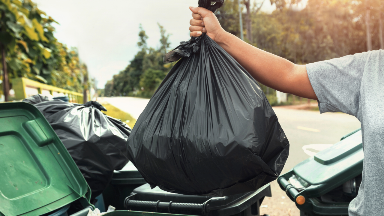A person is putting a black garbage bag into a trash can.