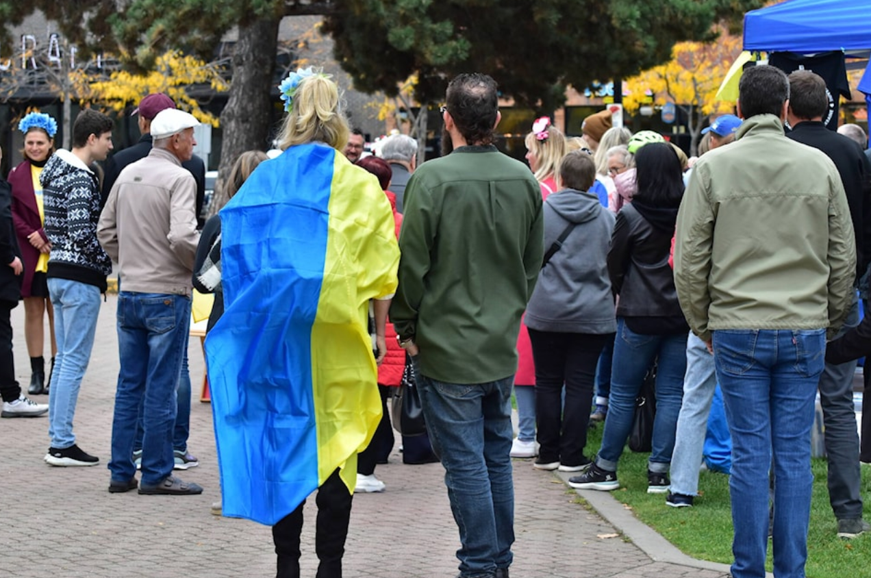Woman walking in a crowd with a Ukrainian flag over her shoulders