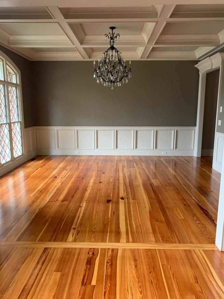 A large empty room with hardwood floors and a chandelier hanging from the ceiling.