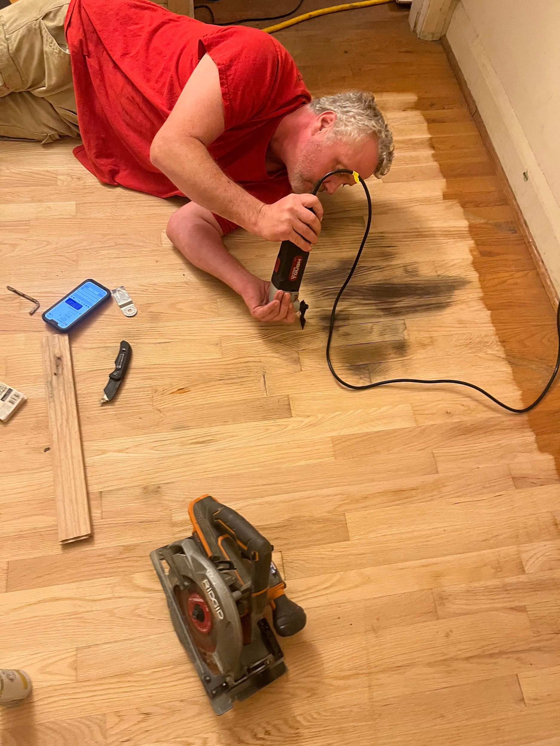 A man is kneeling on the floor using a circular saw.