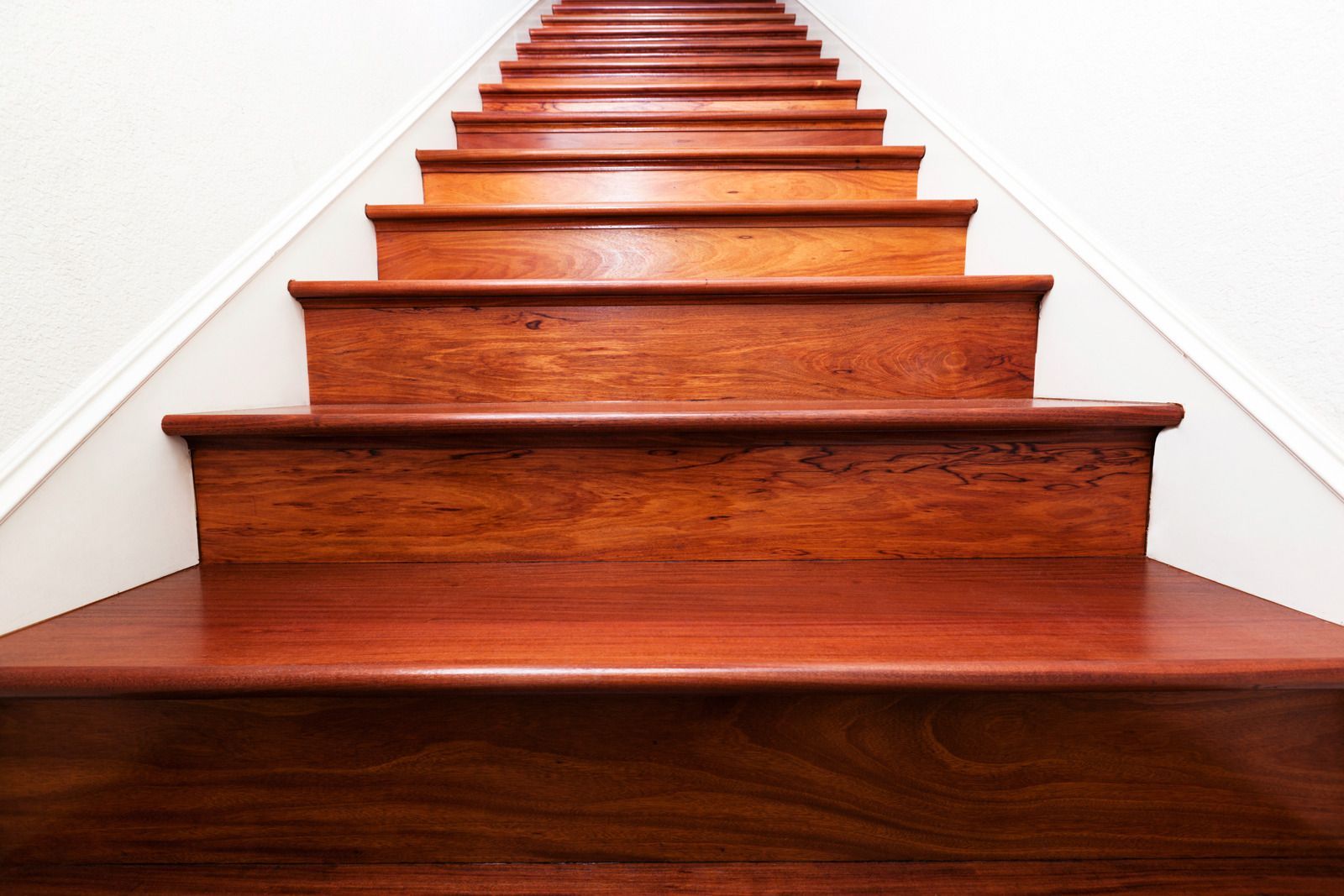 Wooden staircase, ascending against a white wall, viewed from a low angle.