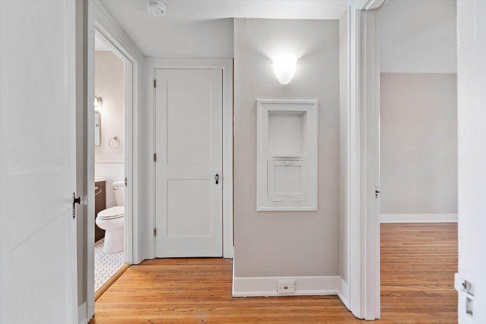 A hallway with hardwood floors and white doors leading to a bathroom.