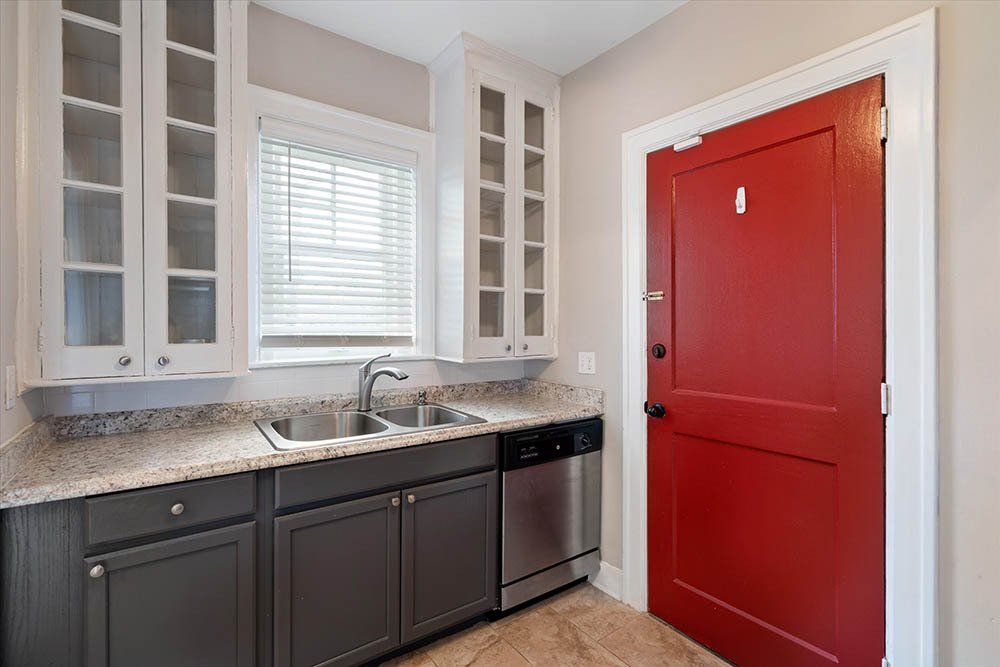 A kitchen with a sink , dishwasher , and red door.