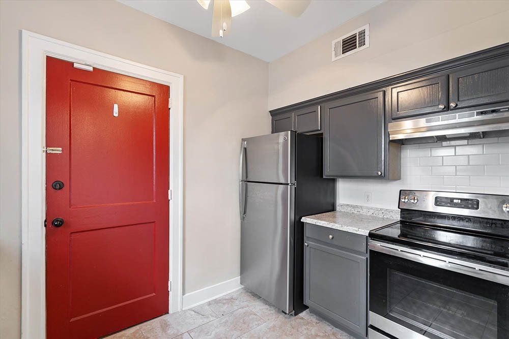 A kitchen with a red door , stainless steel appliances , and a refrigerator.