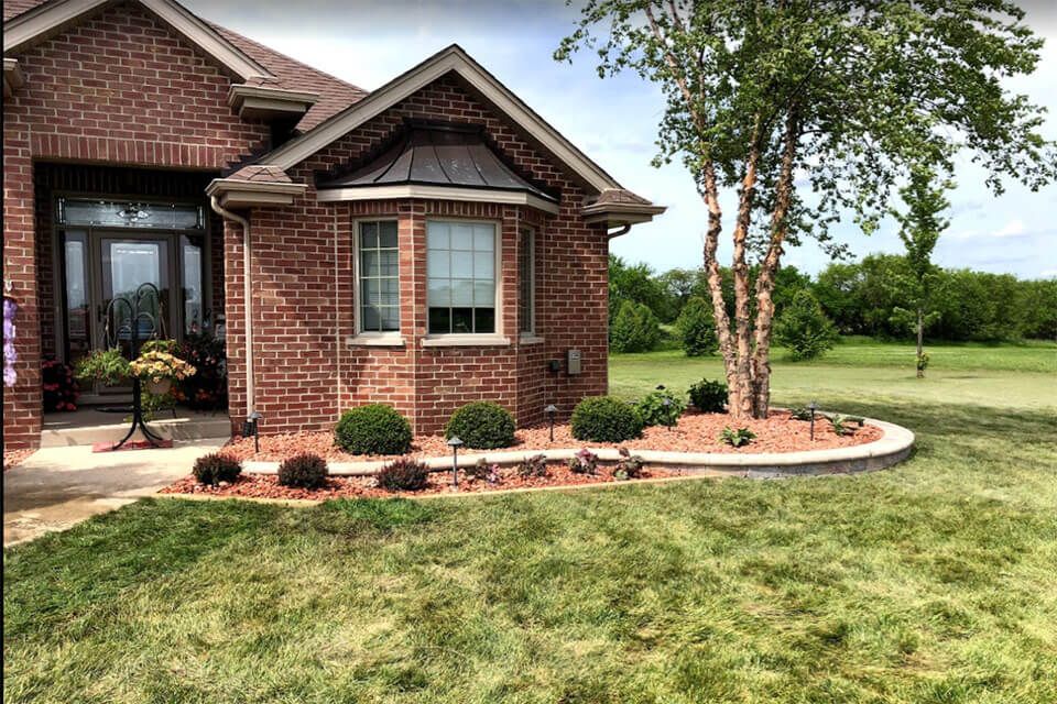 Finished landscape planting renovation with fresh mulch, structured shrubs, and clean bed edges around a residential home
