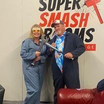 A man and a woman are posing for a picture in front of a super smash room sign.