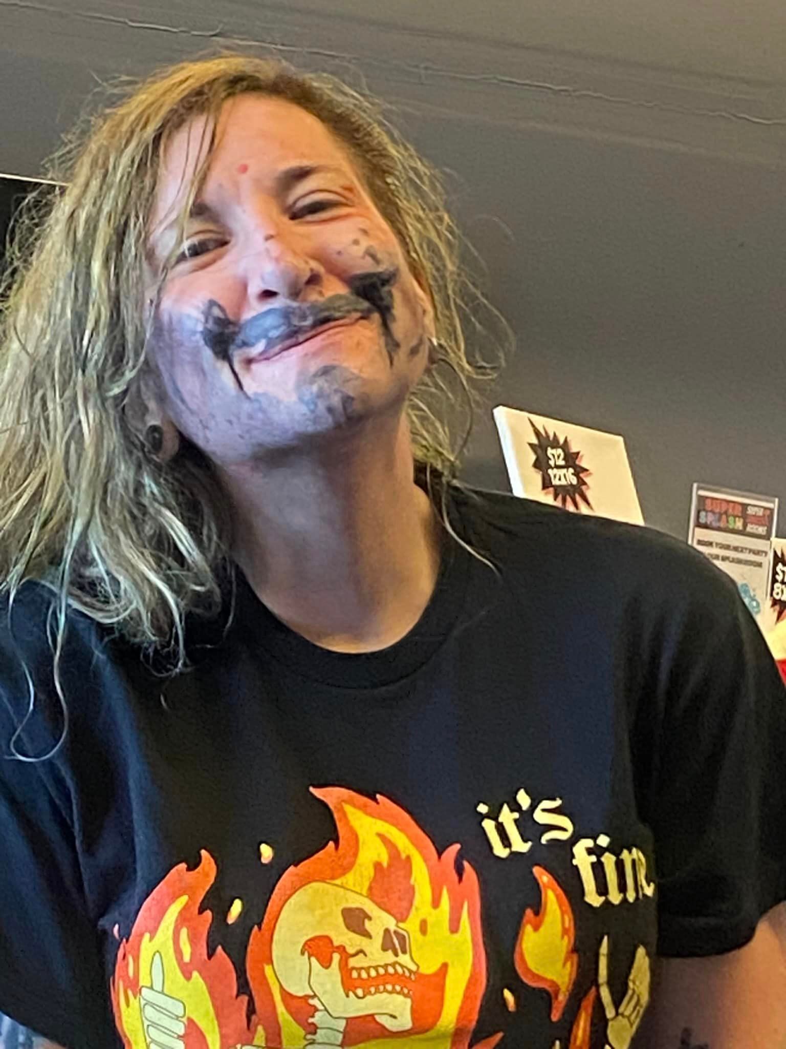A woman wearing a black t-shirt with a skull and flames on it is smiling.