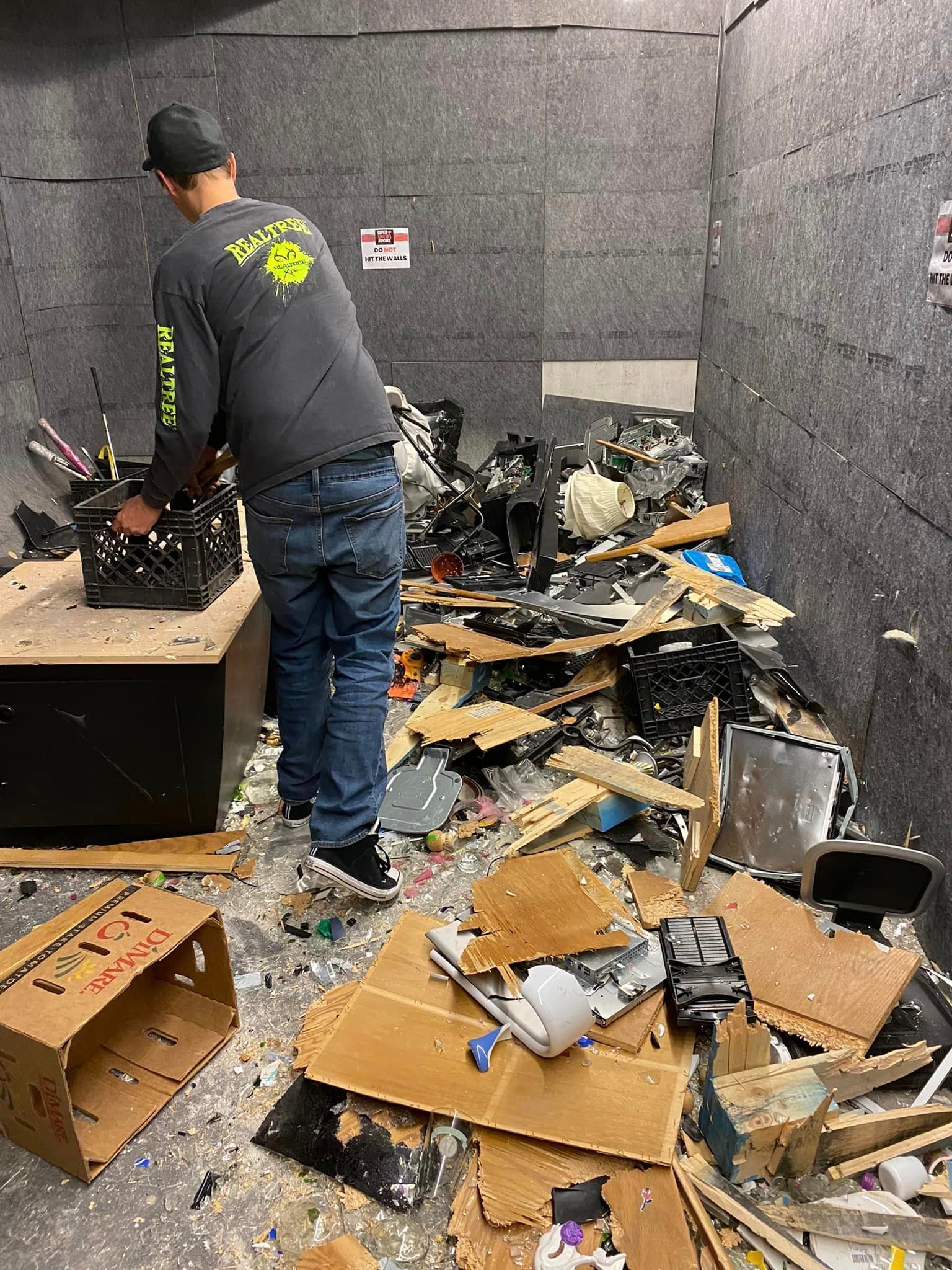 A man is standing in a room filled with cardboard boxes and trash.