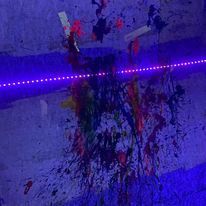 A purple light is shining on a wall with a lot of paint on it.