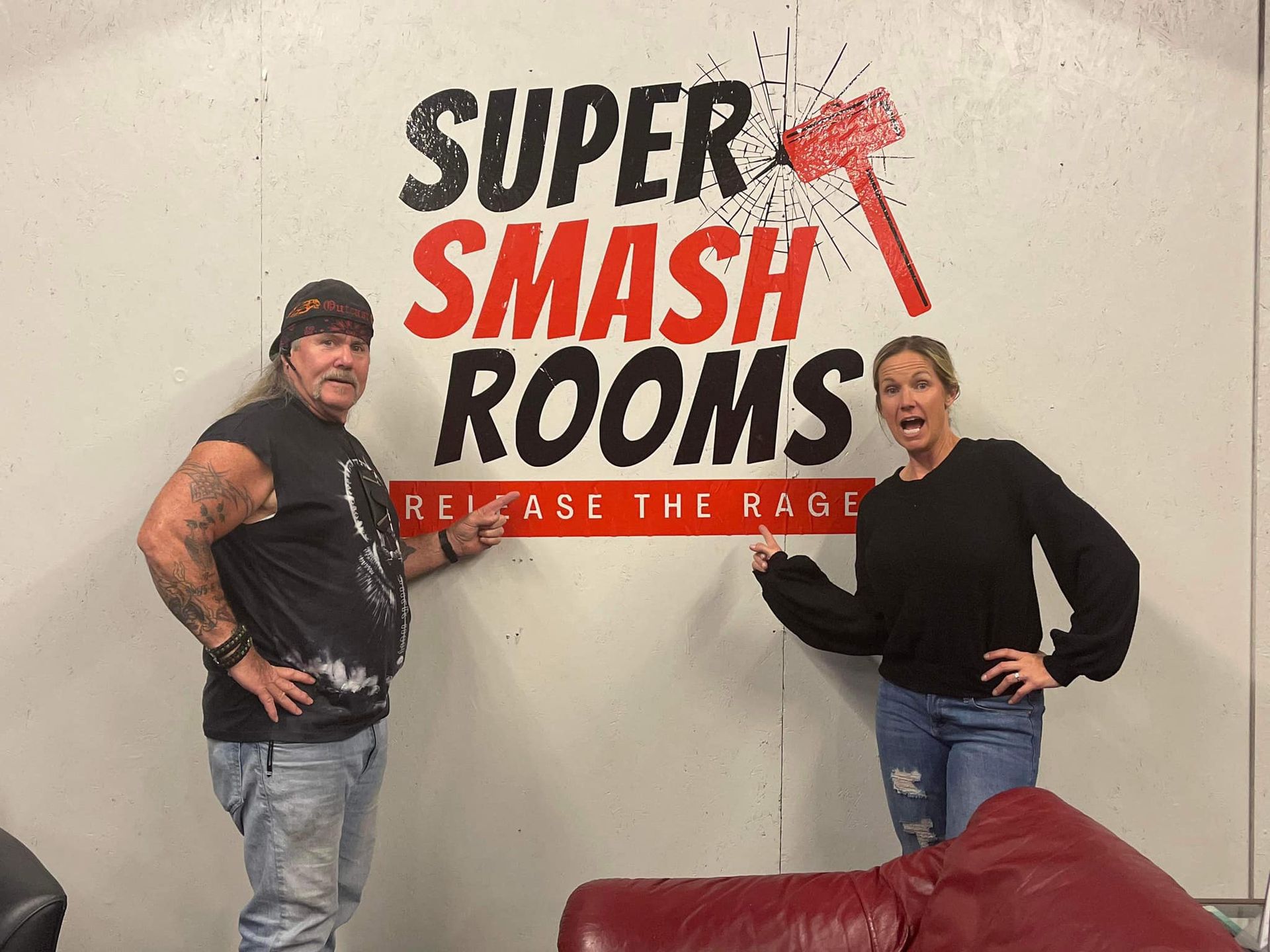 A man and a woman are standing in front of a sign that says super smash rooms.