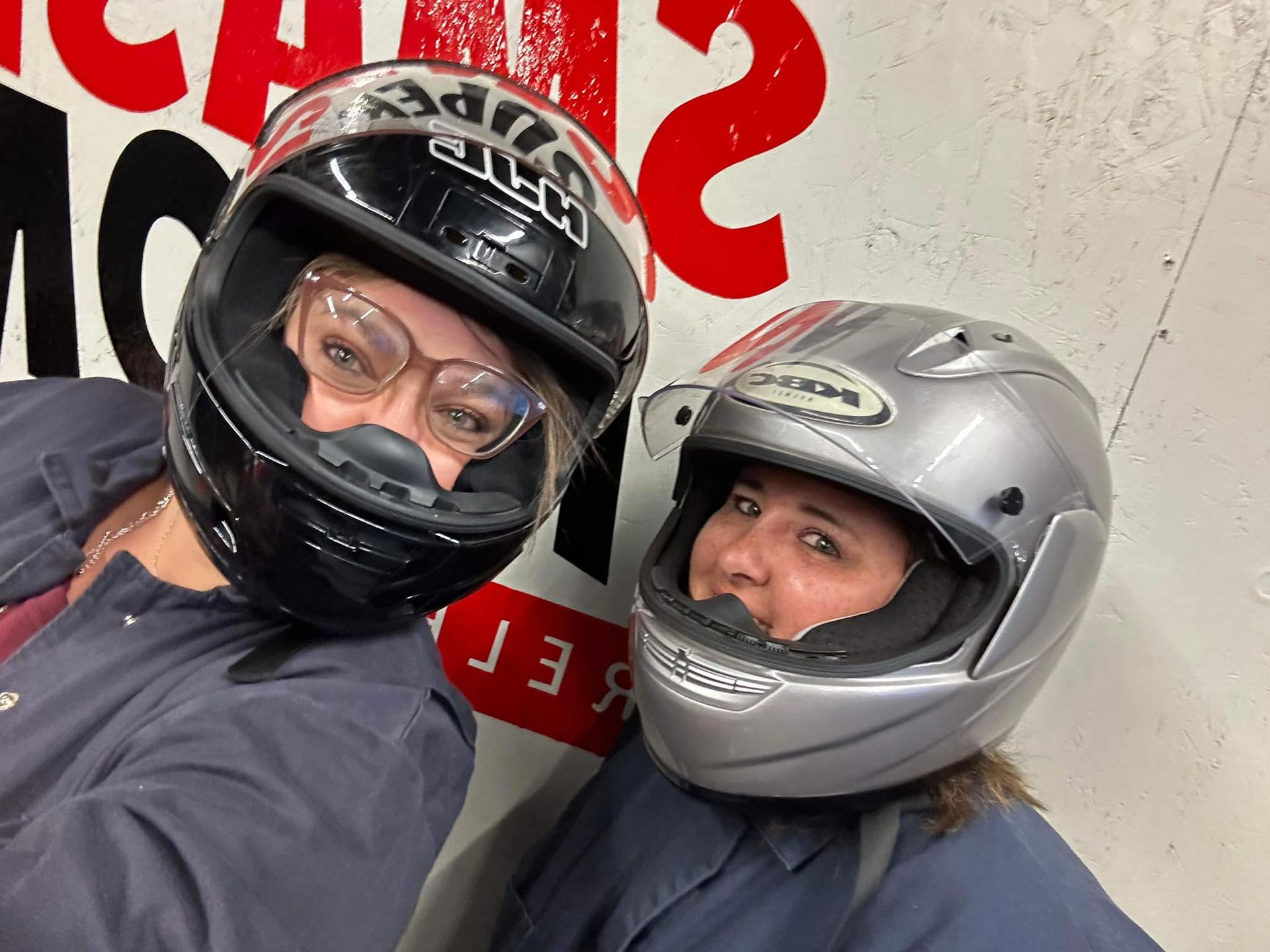 Two women wearing motorcycle helmets pose for a picture