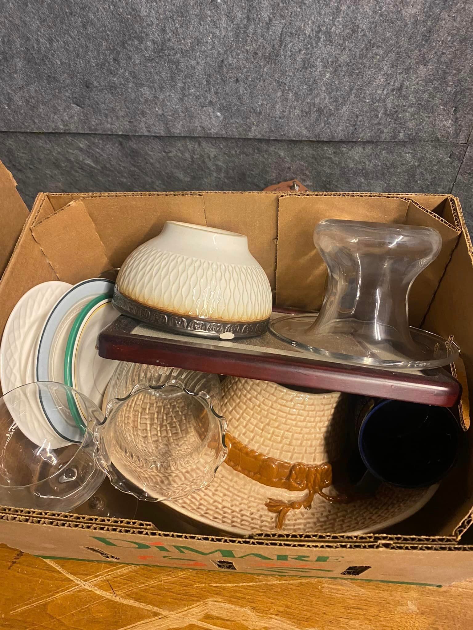 A cardboard box filled with plates , bowls , glasses and a hat.