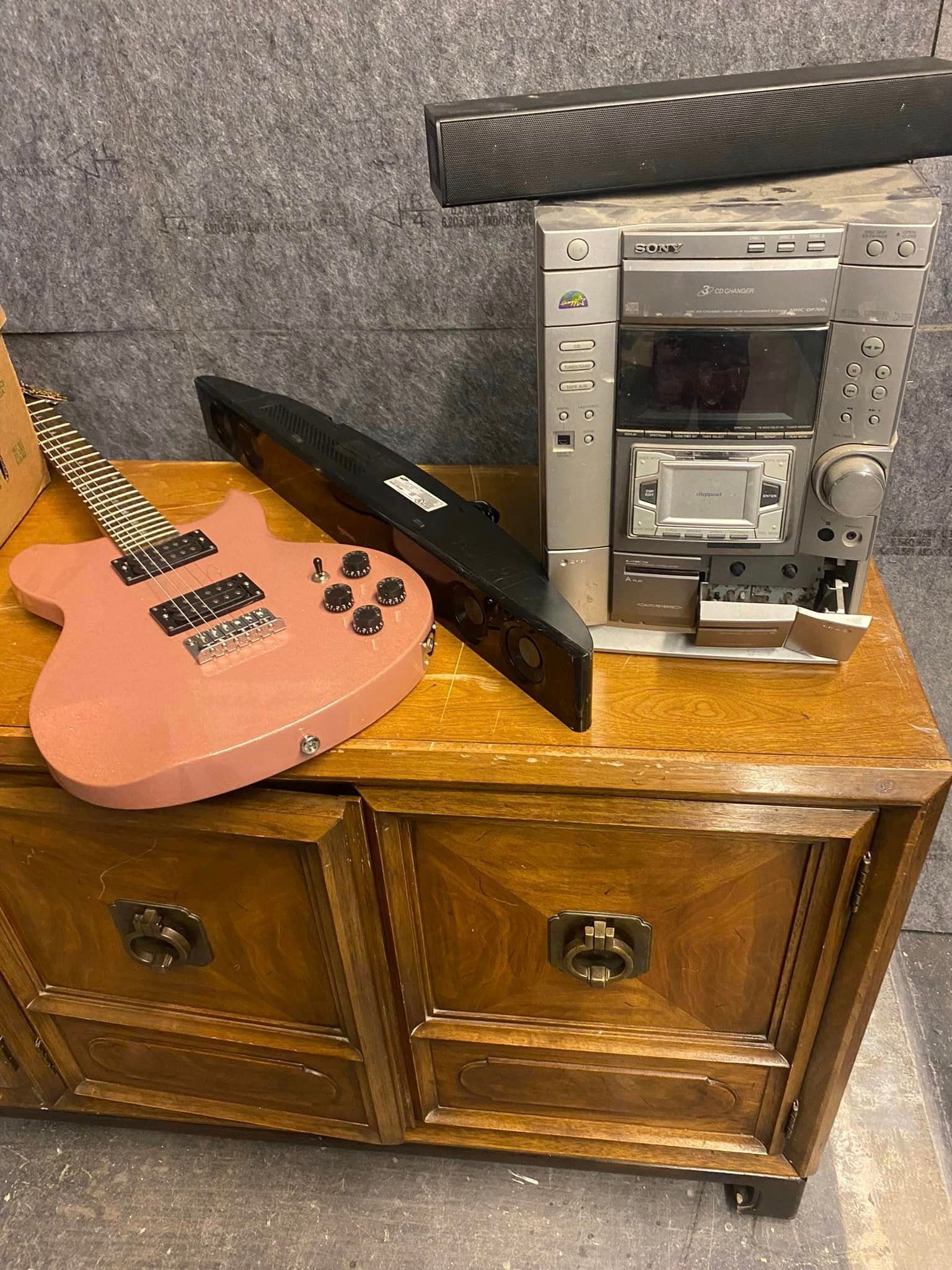 A pink guitar is sitting on top of a wooden dresser next to a stereo.