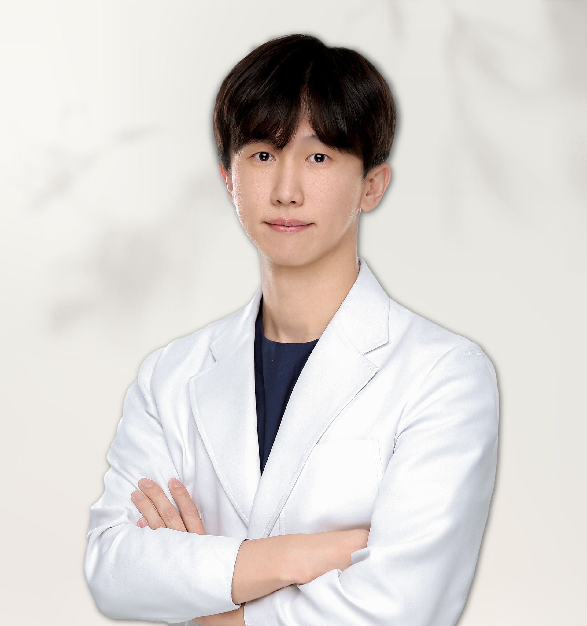 A person wearing a white lab coat and round-rimmed glasses against a light gray background.