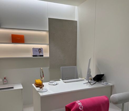 A modern home office with a beige desk, ergonomic chair, built-in shelves with warm lighting, and an integrated sink area.