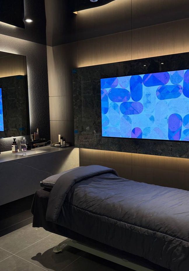 A bright white hallway with marble floors, several closed doors, and overhead cove lighting leading to an exit sign.