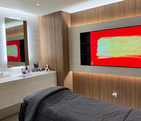 An empty operating table in a room with dark red walls, medical equipment, and a rolling stool.