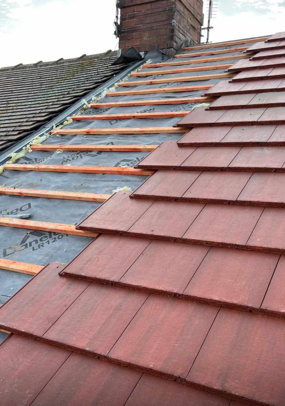 Emergency roof repair in progress with new red tiles being installed alongside old slate tiles, completed by Armstrong Roofing in North Shields.