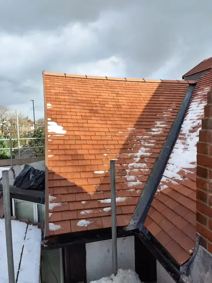 Half-completed pitched roof replacement in progress, showing new red tiles laid next to older ones.