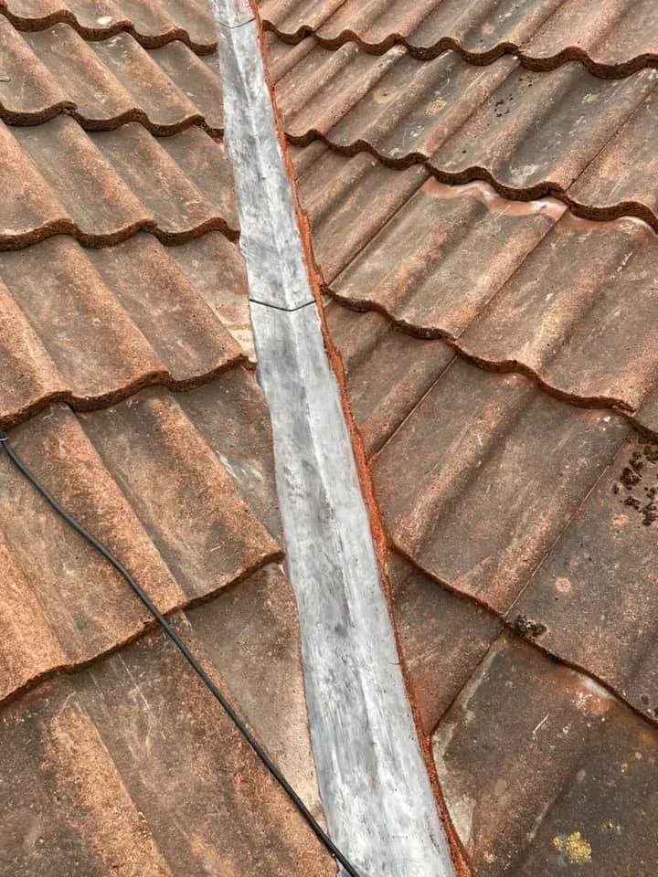Worn red tiled roof section before repairs, showing weathered surface and open valley channel.