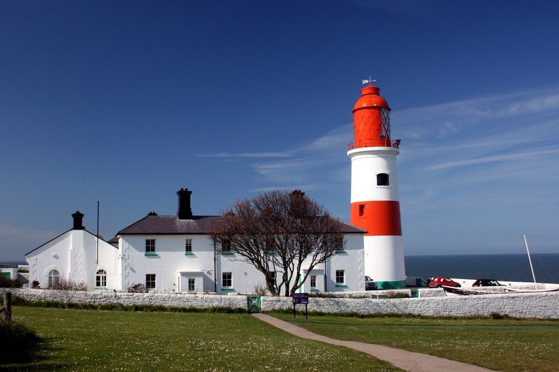 Souter Lighthouse in South Tyneside on a clear sunny day, featuring its iconic red-and-white striped tower, adjacent buildings, and surrounding grassy landscape overlooking the North Sea.