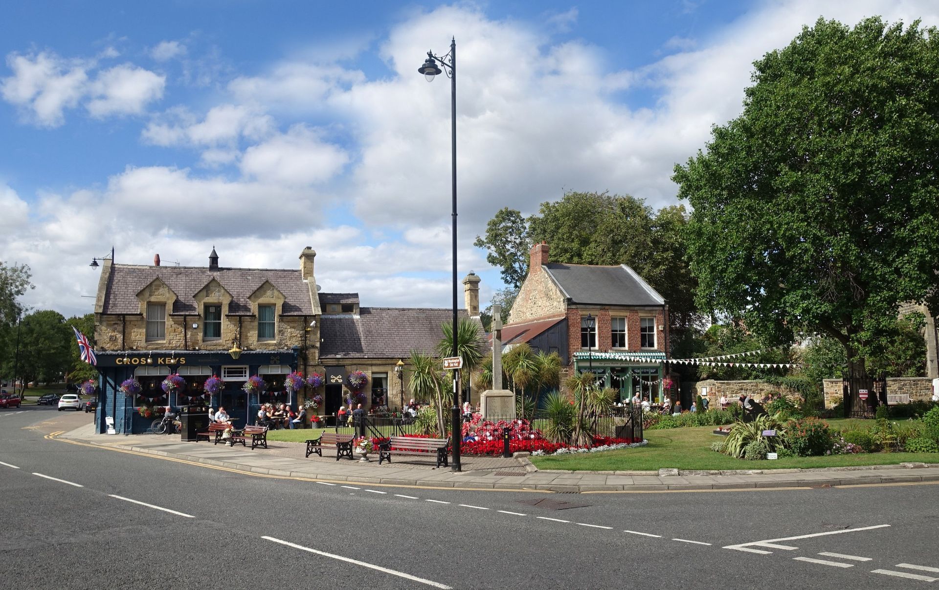 Washington Village Green on a bright sunny day, featuring a historic pub, surrounding shops, lush greenery, and locals enjoying the outdoor seating area in Tyne and Wear.