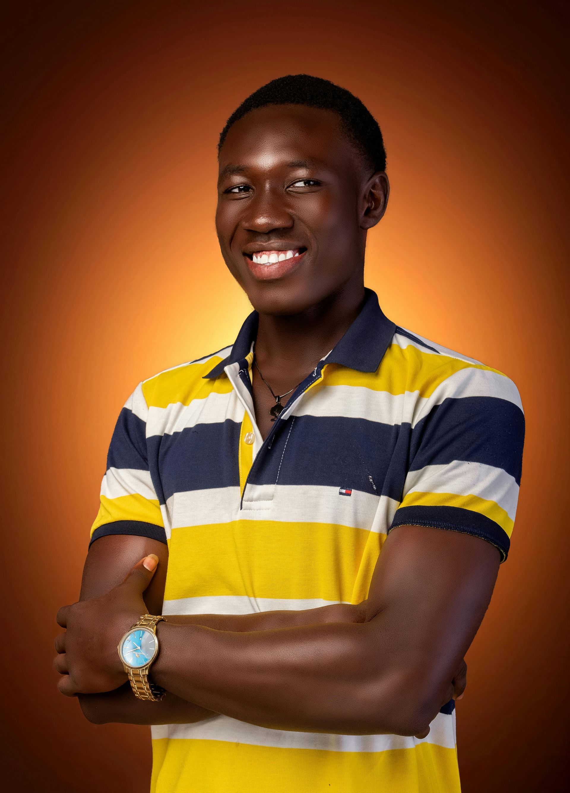 Man in striped polo shirt smiles, arms crossed, wearing a watch. Orange gradient background.