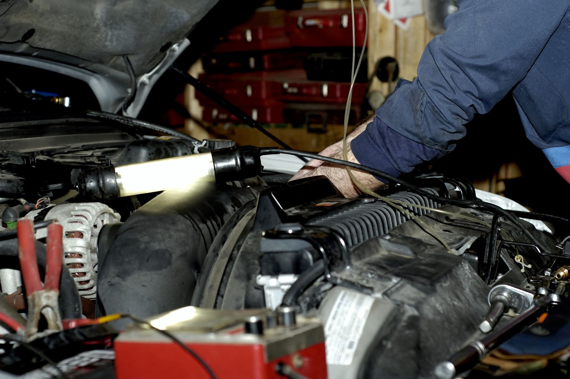 A man is working on a car engine with a flashlight
