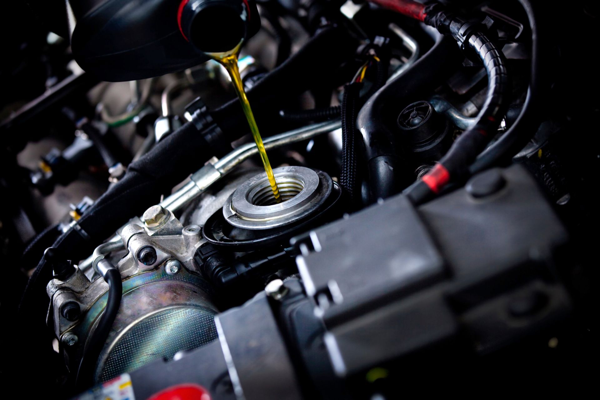 A close up of a person pouring oil into a car engine.