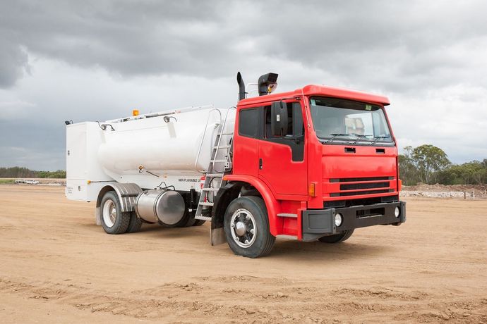 A red and white truck is parked in a dirt field.