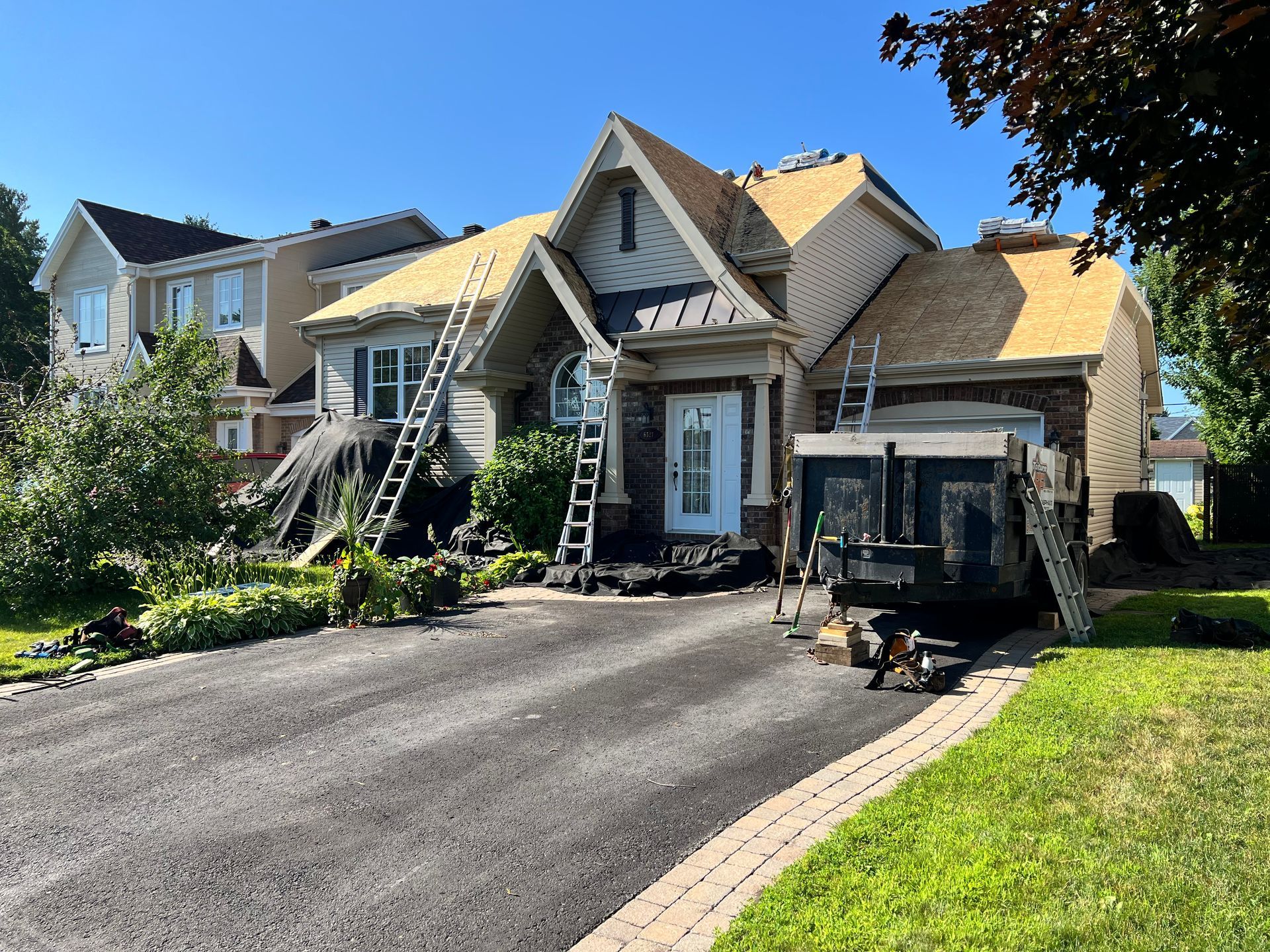 Maison avec toiture partiellement refaite ; échelles et débris sur l'allée asphaltée.