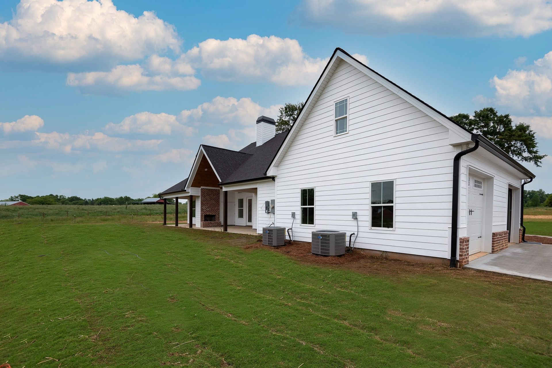 A white house with a black roof is sitting in the middle of a grassy field.