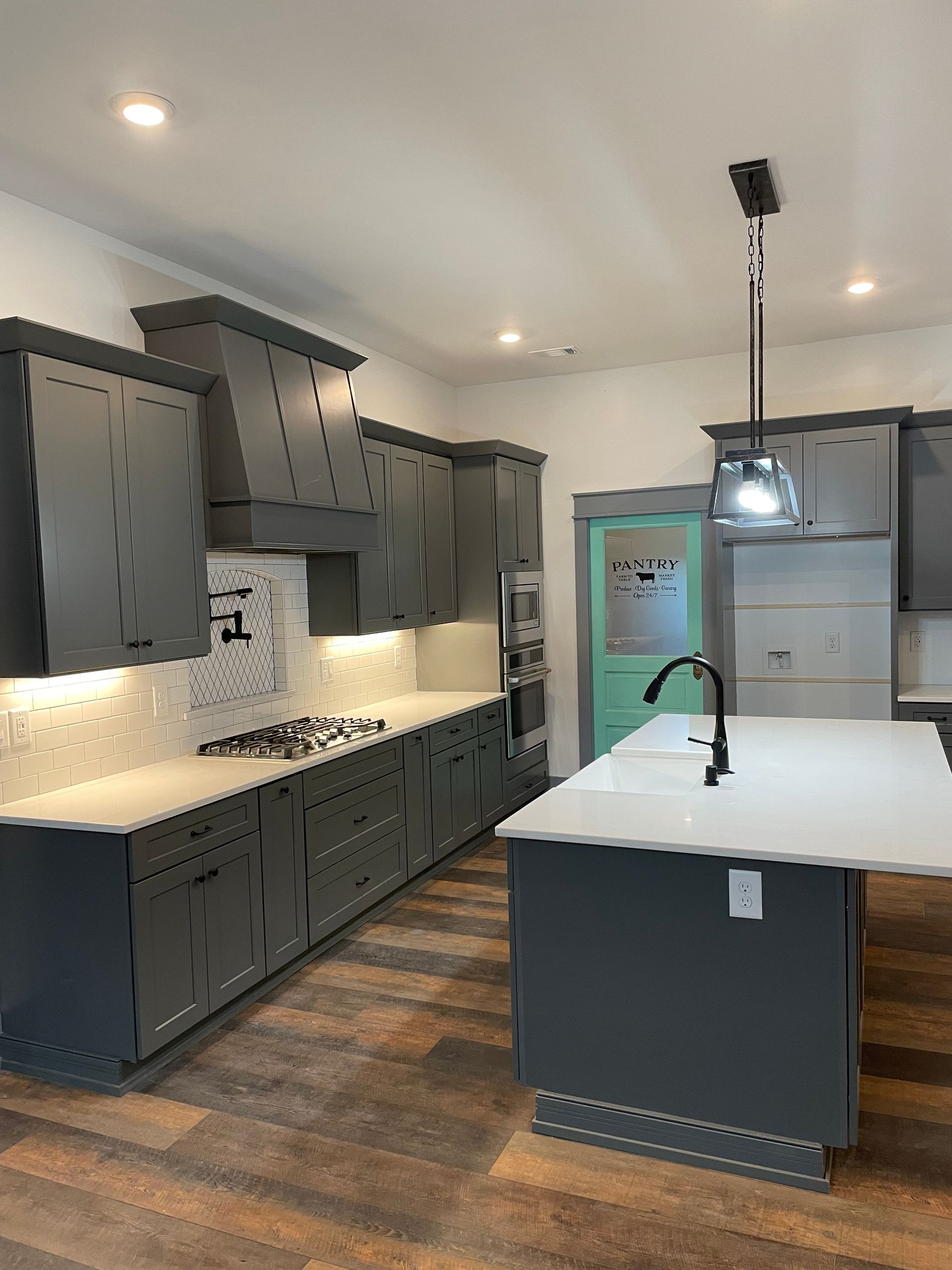 A kitchen with gray cabinets , white counter tops , and a large island.