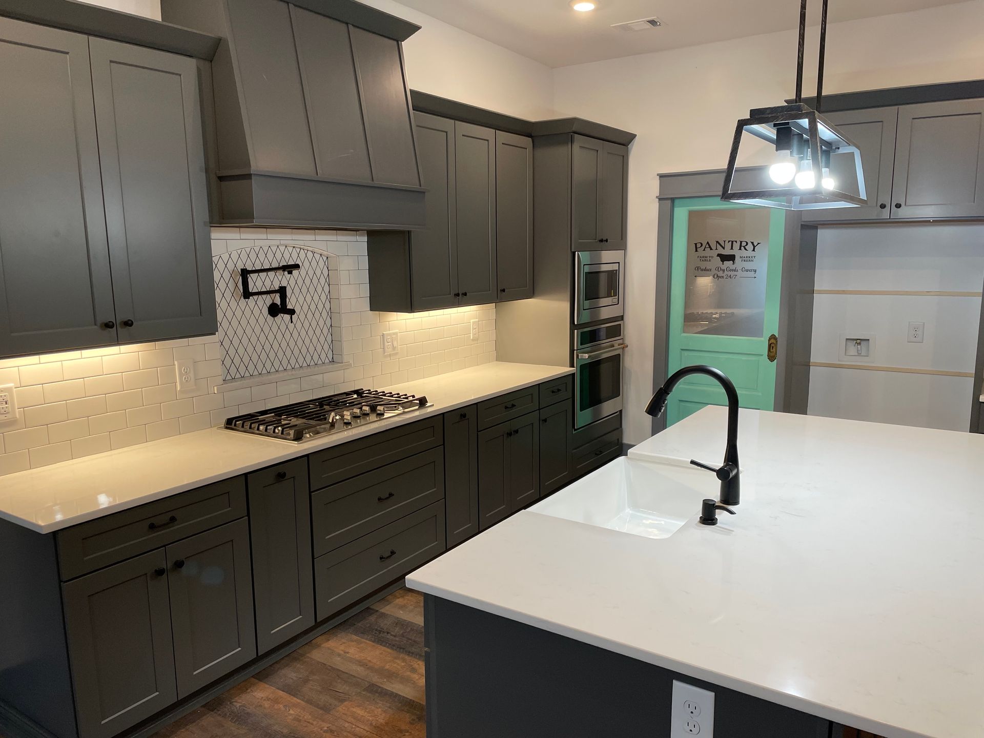 A kitchen with gray cabinets , white counter tops , and a large island.