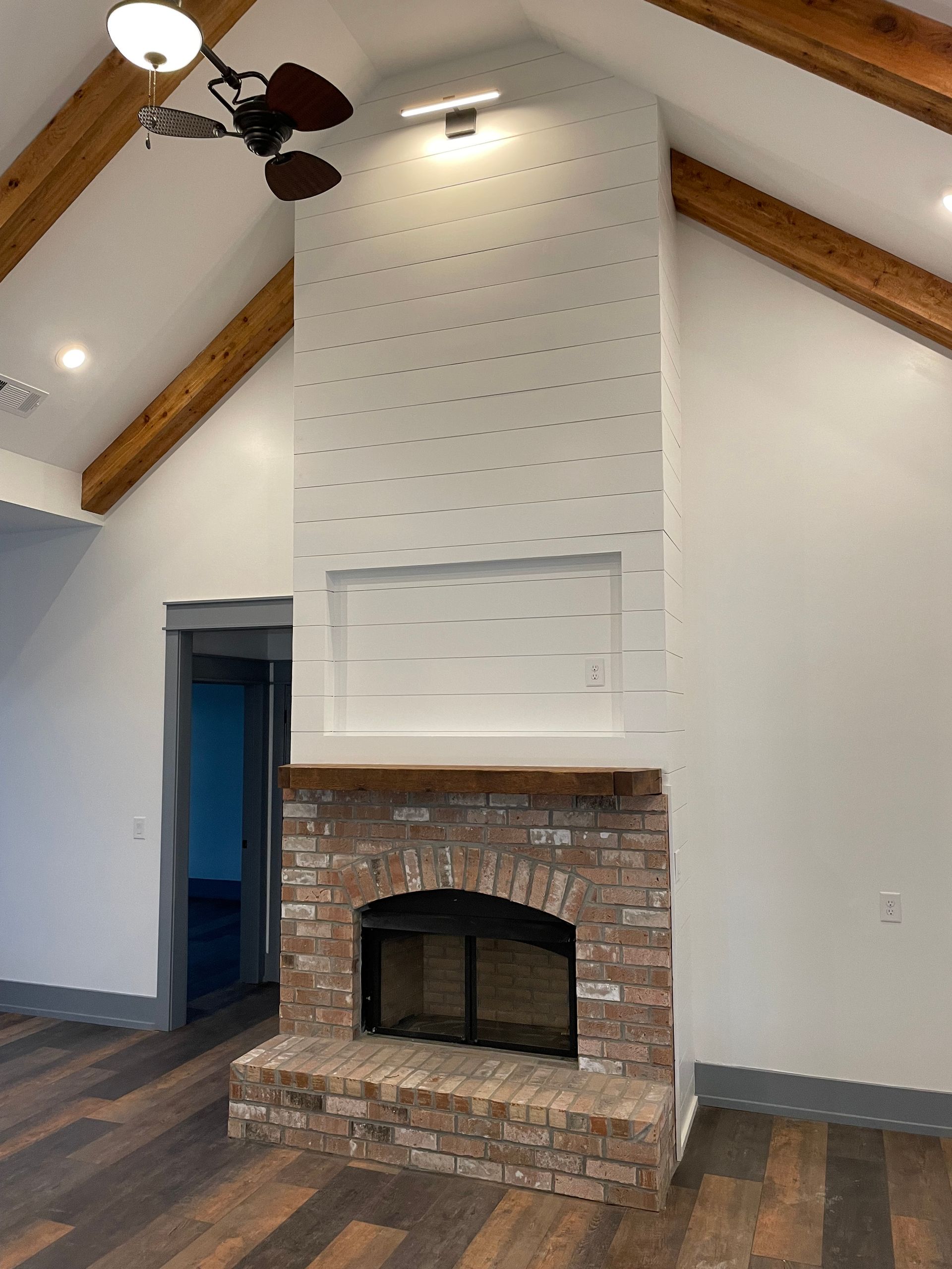 A living room with a brick fireplace and a ceiling fan.