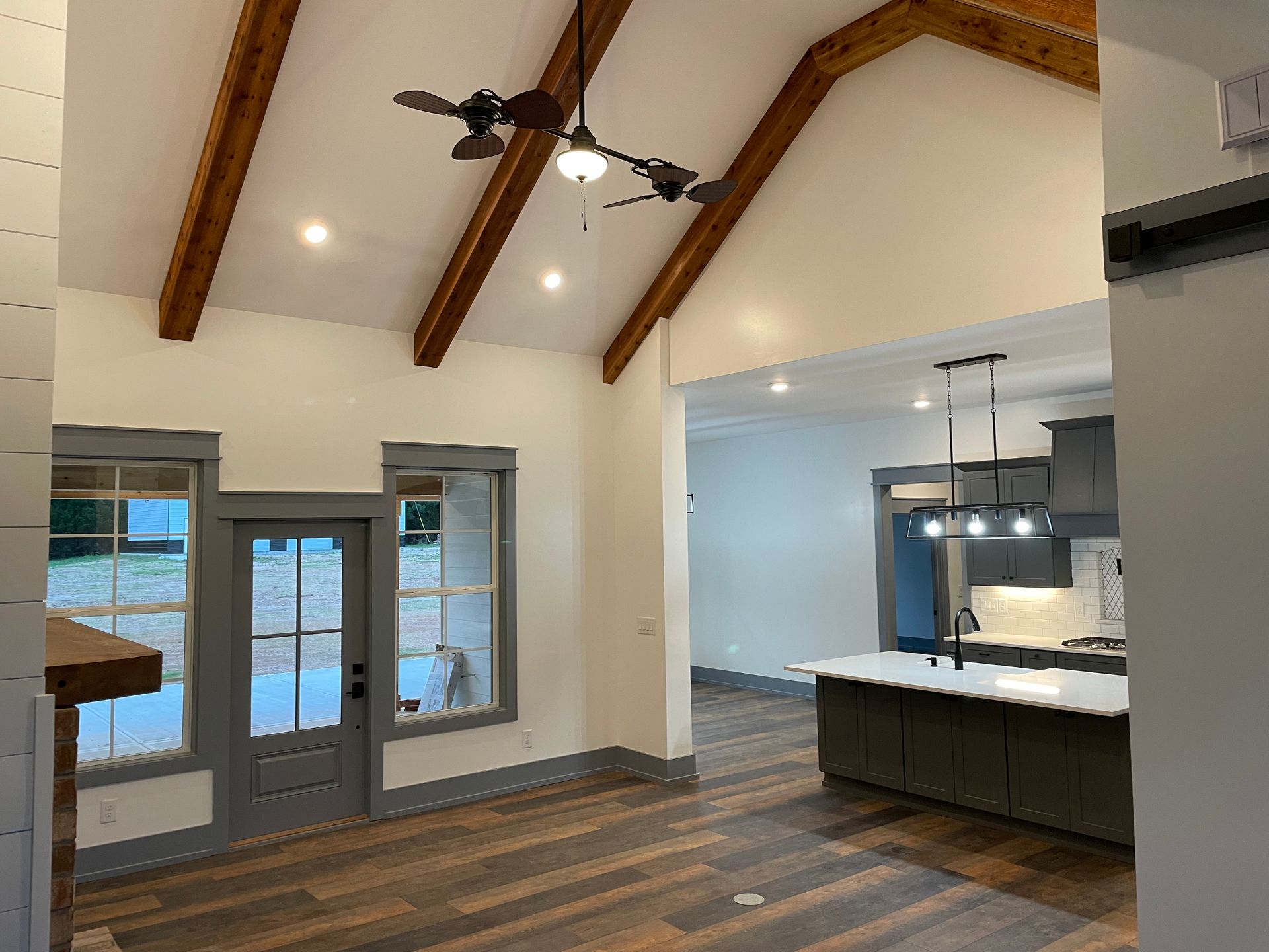 A living room with a ceiling fan and a kitchen in the background.