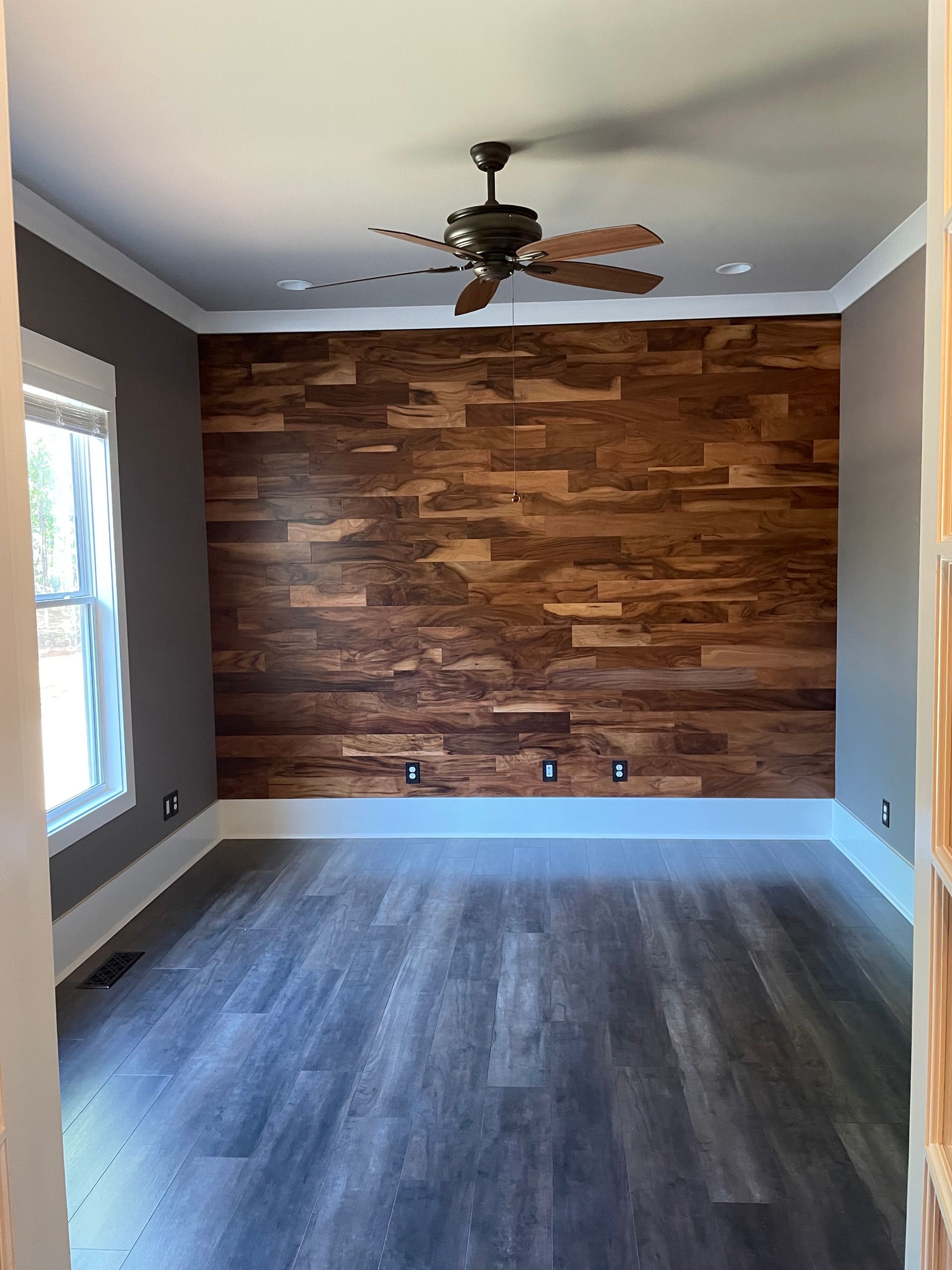An empty room with a wooden wall and a ceiling fan.