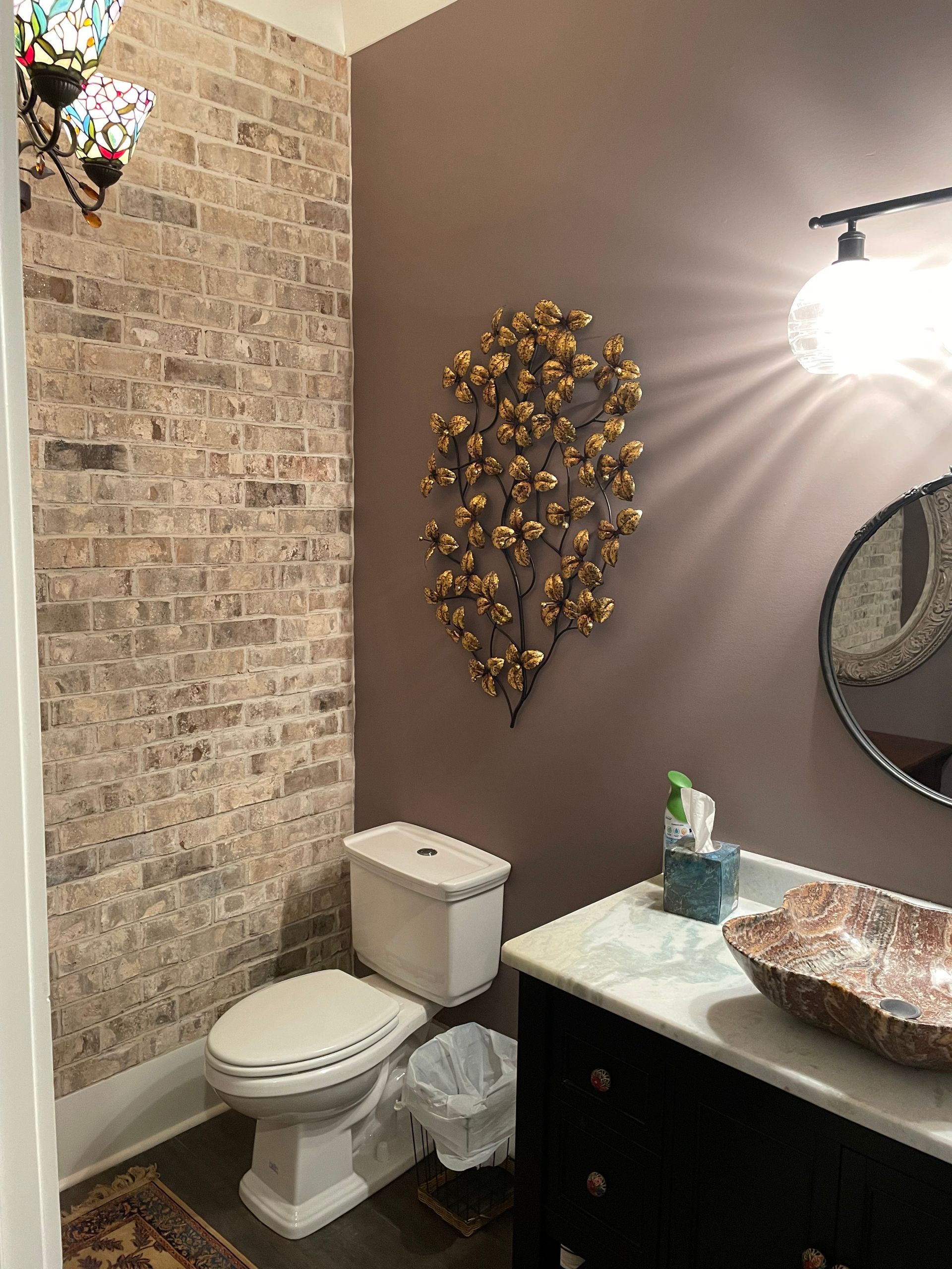 A bathroom with a toilet , sink , mirror and brick wall.