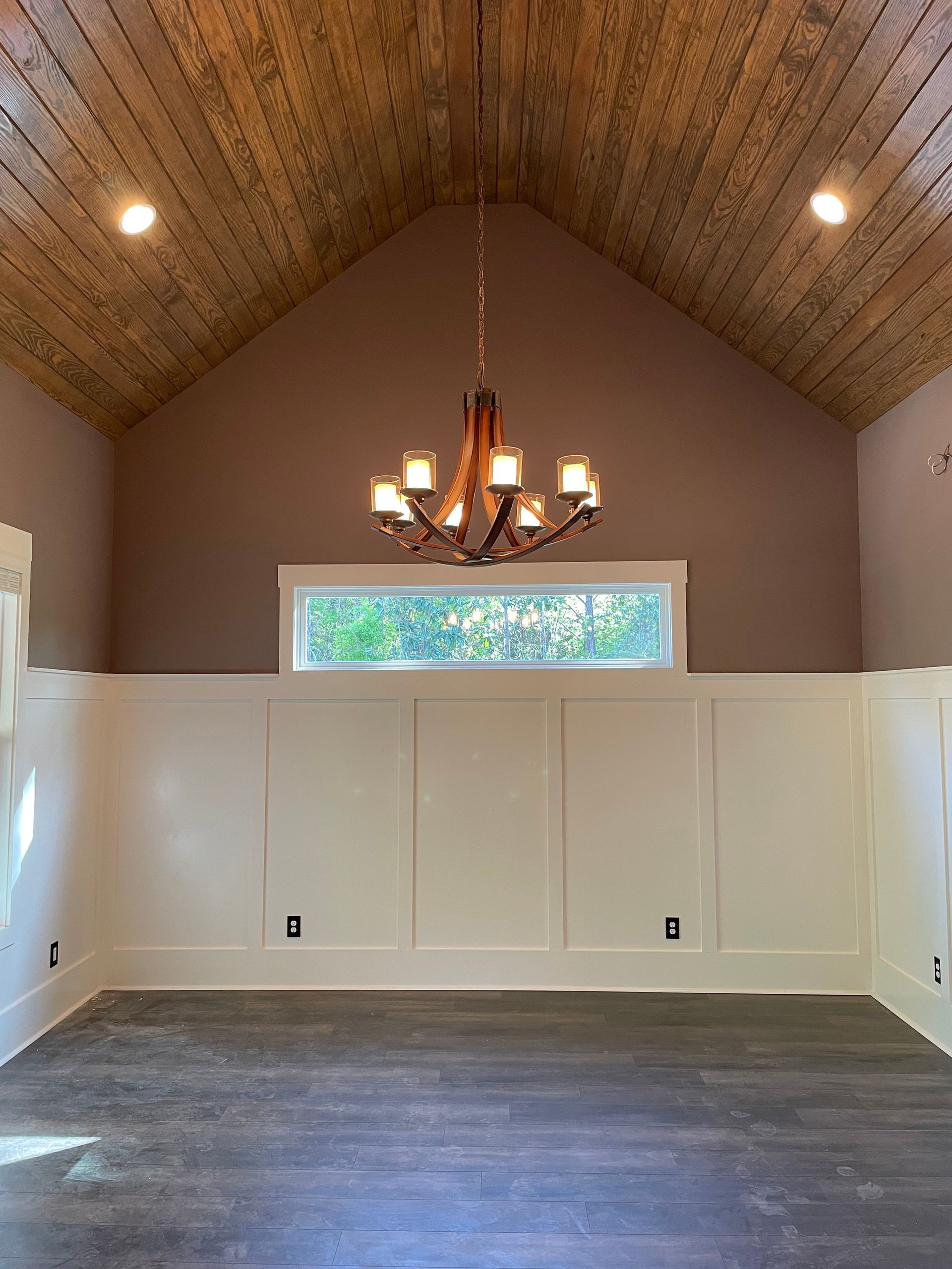 An empty room with a vaulted ceiling and a chandelier hanging from the ceiling.
