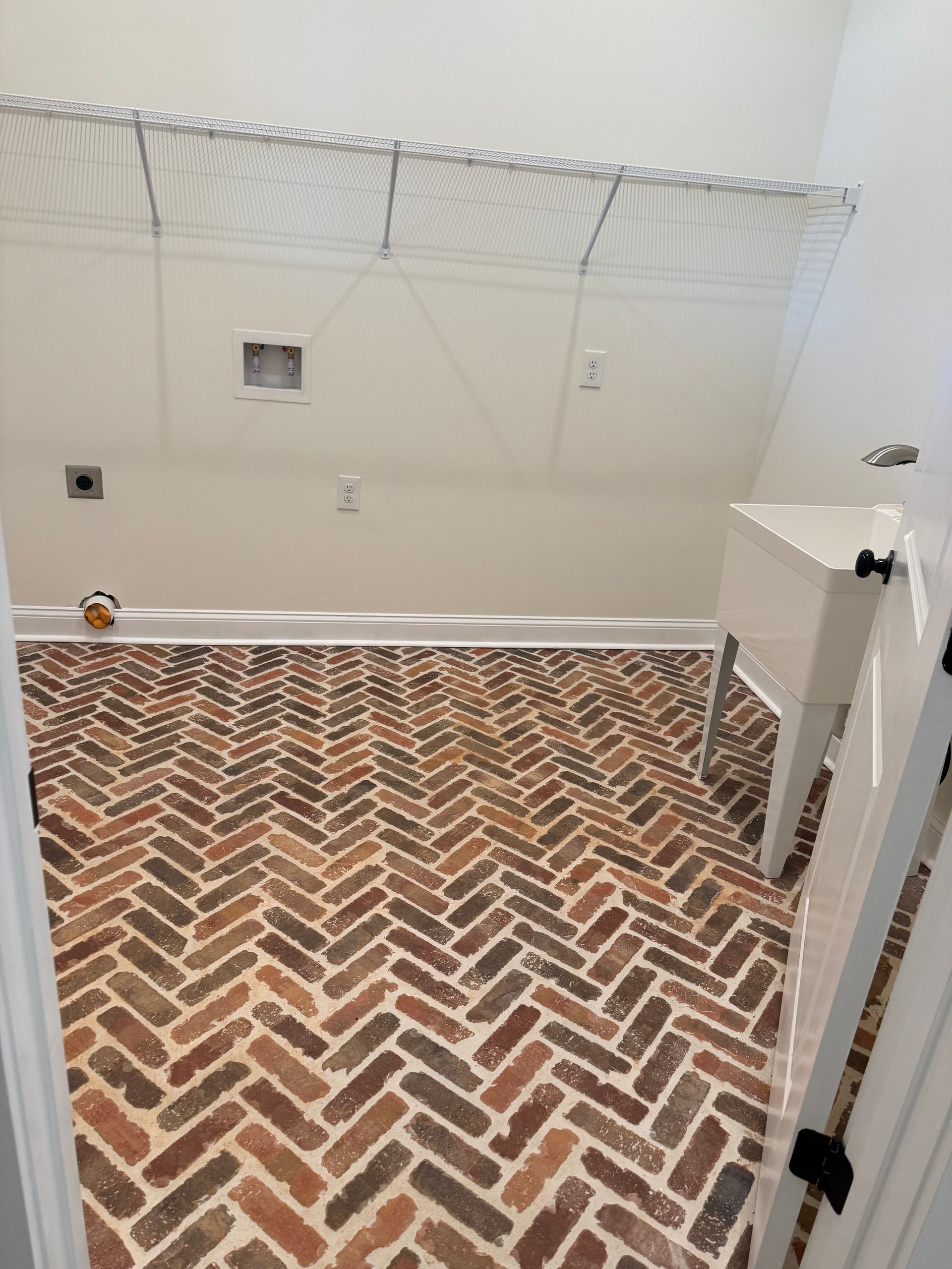 A laundry room with a brick floor and a white sink.